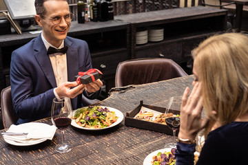 Fototapeta na wymiar handsome adult man presenting valentines day gift to girlfriend at restaurant