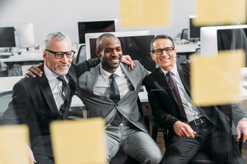 multicultural smiling businessmen looking at notes during meeting in office