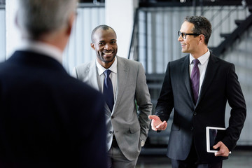 selective focus of smiling multiracial businessmen having conversation while walking in office