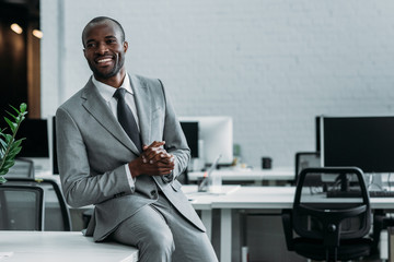 smiling african american businessman sitting on table in office