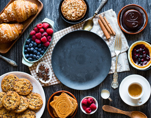 Top view of a wood table full of cakes, fruits, coffee, biscuits, spices and more