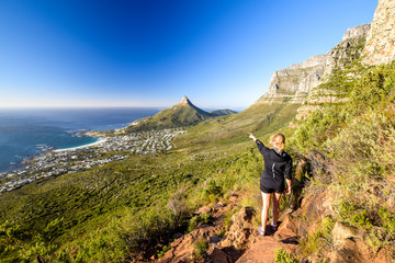 Young female hiker pointing at the suburb of Camps Bay and Lion's Head and Table mountain (right) in Cape Town, South Africa. Seen from Kasteelspoort Hiking Trail, part of Table Mountain National Park