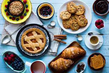 Top view of a wood table full of cakes, fruits, coffee, biscuits, spices and more