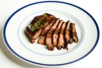 10oz Ribeye steak with thyme and smokey applewood seasoning Sliced and fanned on a blue rim plate on a white background With fork and steak knife