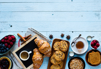 Top view of a wood table full of cakes, fruits, coffee, biscuits, spices and more