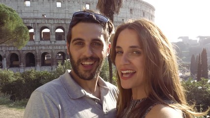 Happy young couple tourists taking selfie video in front of colosseum in rome at sunset with smiling having fun camera point of view pov - Powered by Adobe