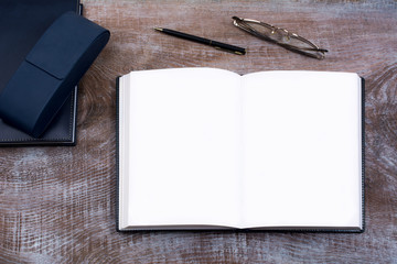 Mockup of open notebook with blank pages, pen, eyeglasses, navy blue case and dairy on the wooden table
