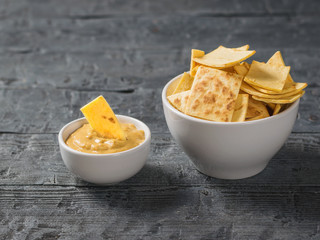 Mexican tortilla chips with cheese in a white bowl on a black wooden table.