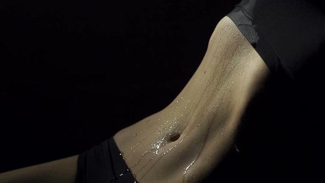 Close-up of wet belly of sexy girl in black underwear on black background. Close-up of erotic wet belly sexy girl who performs sensual dance.
