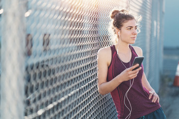 Portrait of sporty woman on the city street doing workout session and using smartphone with music