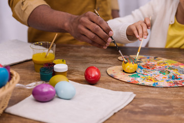 cropped image of african american father and daughter painting easter eggs with poster paints