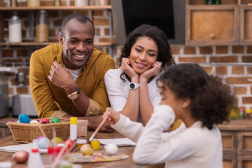 happy african american parents looking how daughter painting easter eggs