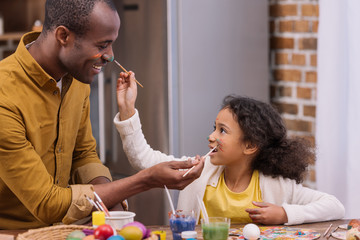 african american father and daughter having fun and painting faces, easter concept