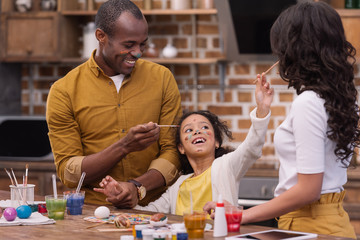 happy african american parents and daughter having fun while painting easter eggs
