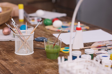 paint brushes and poster paints for easter eggs on wooden table