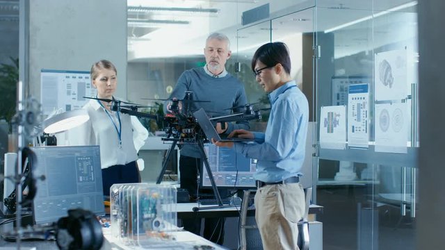 Team of Aviation Engineers Work on a New Drone, Have discussion, Use Laptops. In the Background Scientific Laboratory.