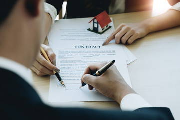Cropped image of real estate agent assisting client to sign contract paper at desk with house model