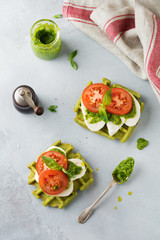 Sandwiches on green wafer with spinach and mozzarella cheese, pesto sauce, tomatoes and basil on a gray concrete old background. Selective focus. Top view.