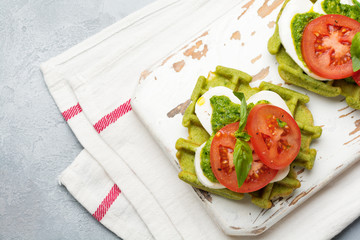 Sandwiches on green wafer with spinach and mozzarella cheese, pesto sauce, tomatoes and basil on a gray concrete old background. Selective focus. Top view.