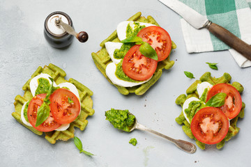 Sandwiches on green wafer with spinach and mozzarella cheese, pesto sauce, tomatoes and basil on a gray concrete old background. Selective focus. Top view.
