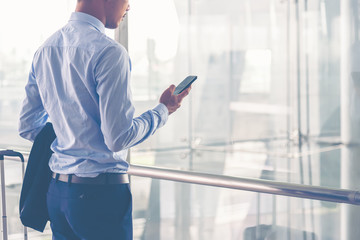 Businessman with a baggage talking via mobile phone at the airport. Businessman wearing suit jacket indoors. A man standing with a baggage using a smart phone in airport departure terminal. 