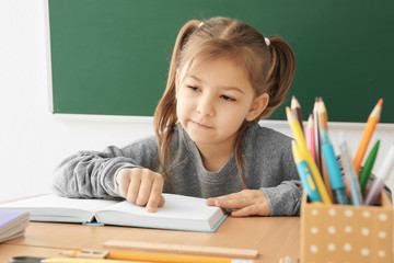 Cute little girl doing homework in classroom