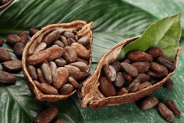 Halves of cocoa pod with beans and green leaves on wooden background - obrazy, fototapety, plakaty