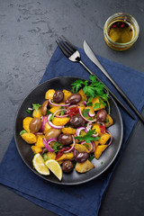 Warm potato salad with olives, pepper, parsley and red onion on black ceramic plate on dark concrete background. Selective focus. Top view. Copy space.