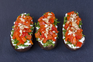 Three eggplants stuffed with cream cheese, green herbs, grilled red and yellow peppers on a black slate background, close up