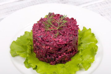 Appetizer, healthy eating, delicious red beet salad with dried plums, walnuts, green lettuce on white plate in wooden table. Dieting and vegetarian concept