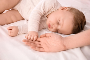 Sleeping baby holding mother's hand on bed