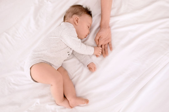 Sleeping baby holding mother's hand on bed