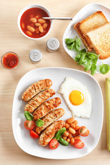 Plate with delicious grilled sausages and fried egg on wooden background