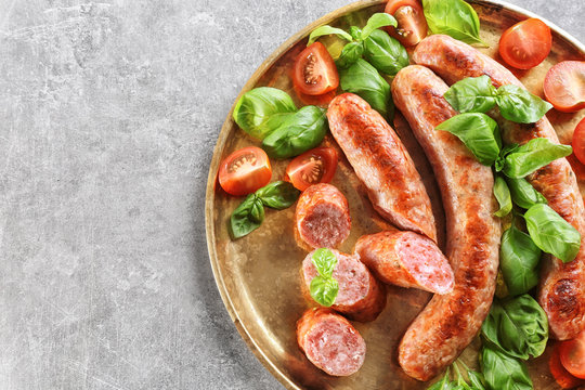 Plate with delicious grilled sausages, tomato and basil on grey background