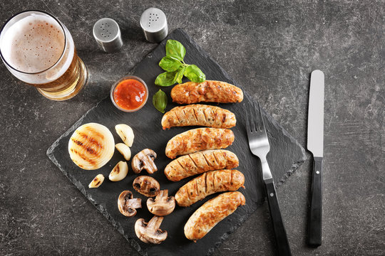 Slate plate with delicious grilled sausages and vegetables on dark background