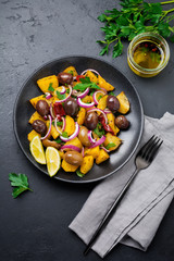 Warm potato salad with olives, pepper, parsley and red onion on black ceramic plate on dark concrete background. Selective focus. Top view. Copy space.