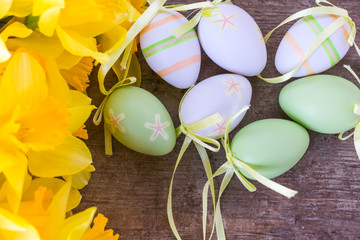 Top view of bright yellow daffodils flowers and easter eggs decorations on old rustic vintage wooden background, spring or easter decoration concept