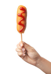 Woman holding tasty corn dog with ketchup on white background