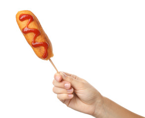 Woman holding tasty corn dog with ketchup on white background