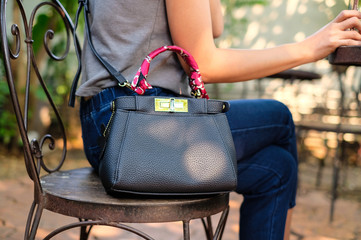 A asian woman wearing blue jeans is shoulder a black handbag was hand Hold the smartphone sitting on the chair in the garden