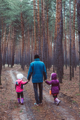 Father and two children walking along the road in a pine forest