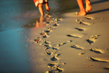mother and daughter walking on beach leaving footprint in sand
