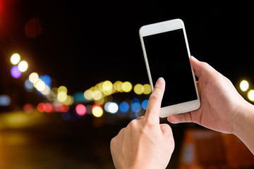 Hand touch screen on smartphone device with night bokeh.