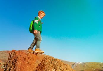 little boy with backpack hiking in mountains