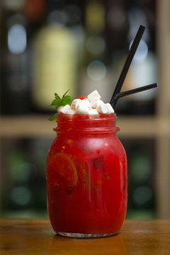 Red smoothies with marshmallow on wooden bar counter. On background rack with bottles.