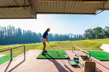 Young woman practices her golf swing on driving range, view from behind,Young girls practicing driving range..
