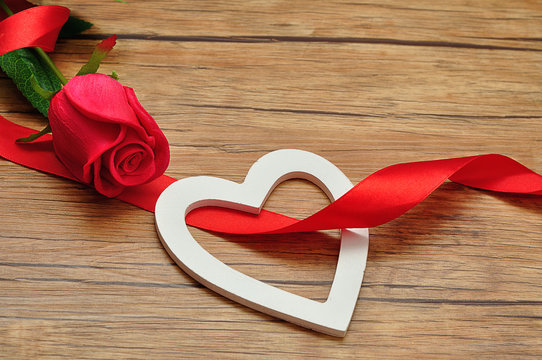 A white wooden heart with a red ribbon and red rose
