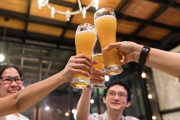 Group of asian friends are clinking or toasting with glasses of light beer at the restaurant. Young people hands toasting and cheering aperitif beers half pint. friendship and celebration concept.