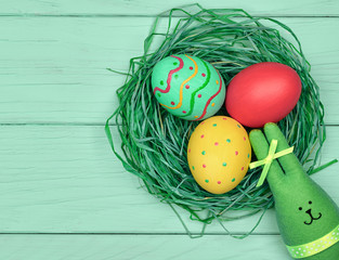 Easter Eggs and Rabbit. Happy Bunny handmade and hand painted Colorful decorated eggs on green straw nest, blue wood. Holiday greeting card