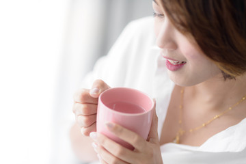 Beautiful woman holding pink cup near window at home.